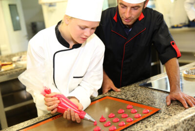 Student in pastry making cookies with help of teacher
